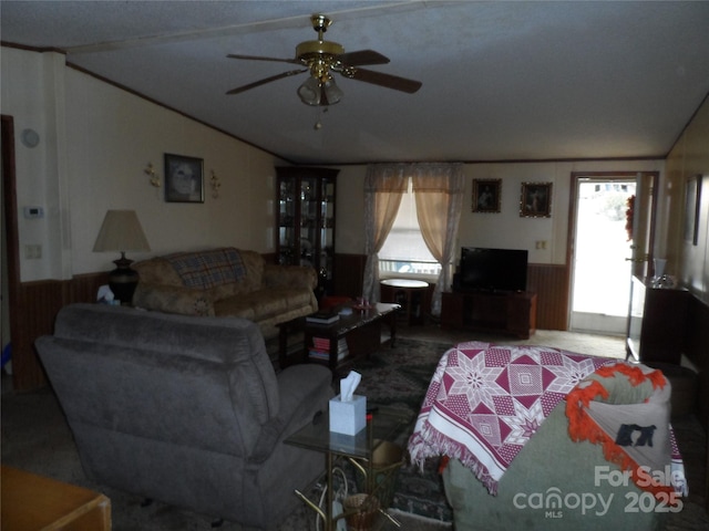 living room with a wainscoted wall, lofted ceiling, wood walls, and a ceiling fan