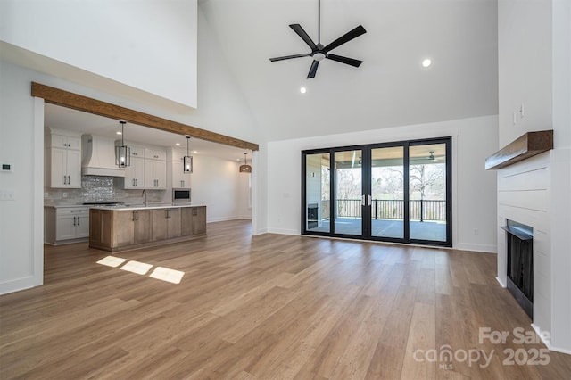 unfurnished living room featuring light wood-style flooring, a fireplace, high vaulted ceiling, a ceiling fan, and a sink