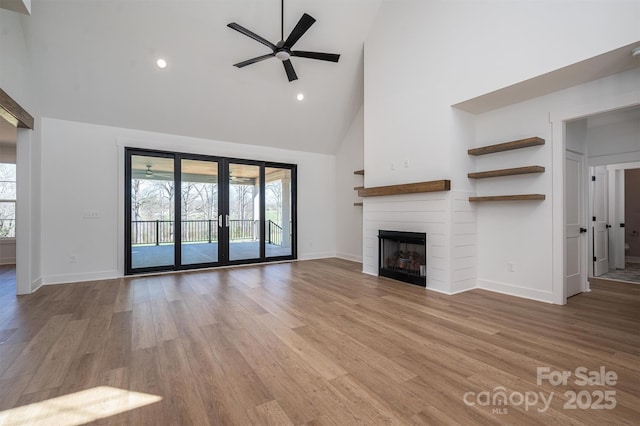 unfurnished living room with a fireplace, wood finished floors, a ceiling fan, and a wealth of natural light