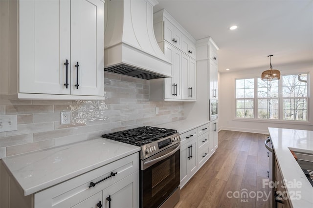 kitchen featuring stainless steel gas range oven, backsplash, light stone counters, light wood-style floors, and custom exhaust hood