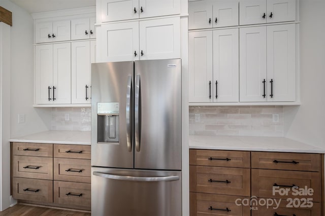 kitchen featuring tasteful backsplash, light stone countertops, brown cabinets, stainless steel refrigerator with ice dispenser, and white cabinets