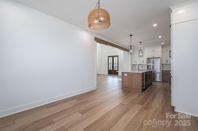 kitchen with light wood-style flooring, an island with sink, tasteful backsplash, stainless steel fridge, and light countertops