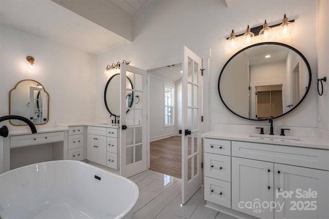 bathroom with a sink, french doors, a soaking tub, and two vanities