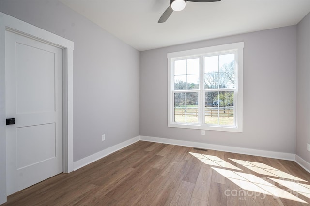 empty room with a ceiling fan, wood finished floors, visible vents, and baseboards