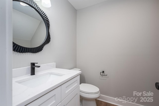 half bath with vanity, toilet, wood finished floors, and baseboards