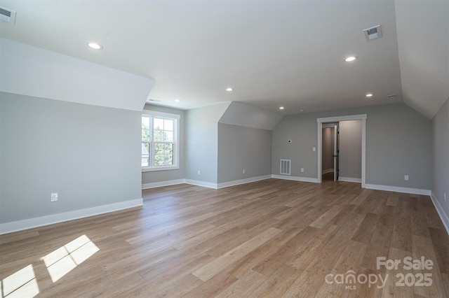 additional living space with vaulted ceiling, light wood-style floors, visible vents, and baseboards