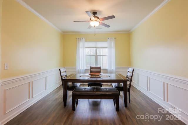 dining area featuring dark wood-style floors, wainscoting, crown molding, and a ceiling fan