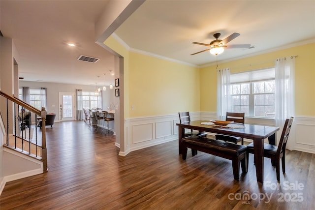 dining room featuring visible vents, crown molding, dark wood-type flooring, a wainscoted wall, and stairs