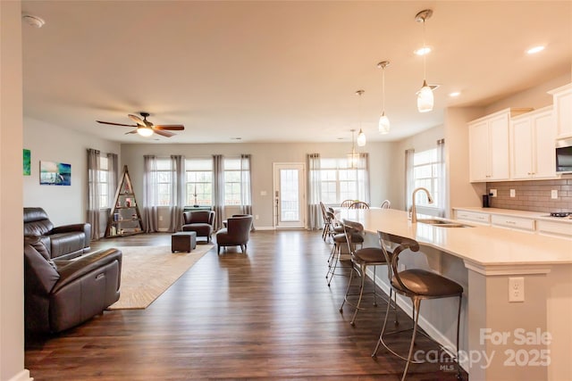 kitchen featuring dark wood finished floors, open floor plan, a breakfast bar area, an island with sink, and a sink