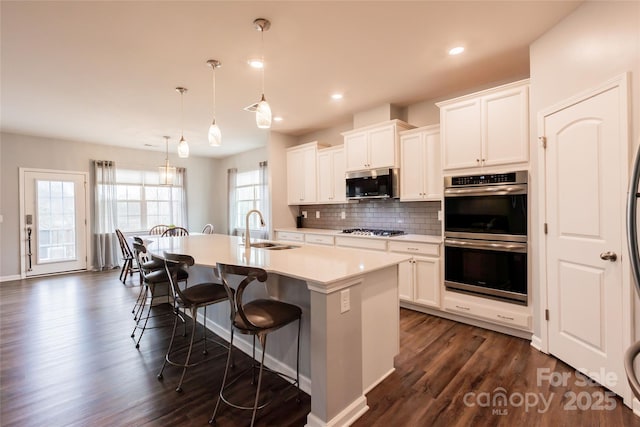 kitchen featuring an island with sink, decorative backsplash, appliances with stainless steel finishes, a kitchen breakfast bar, and a sink