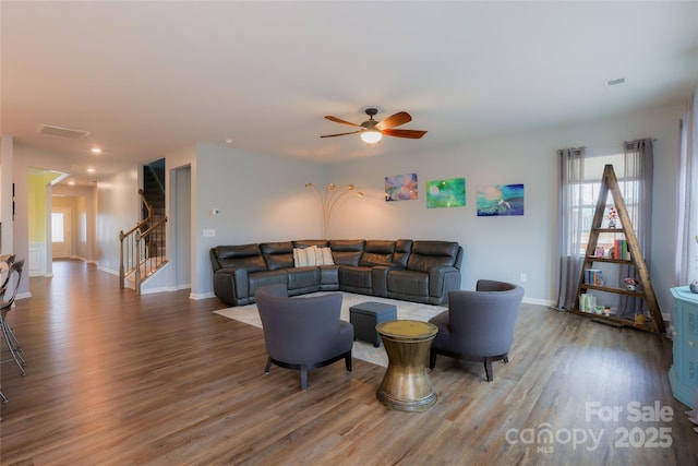 living room featuring visible vents, wood finished floors, stairway, baseboards, and ceiling fan