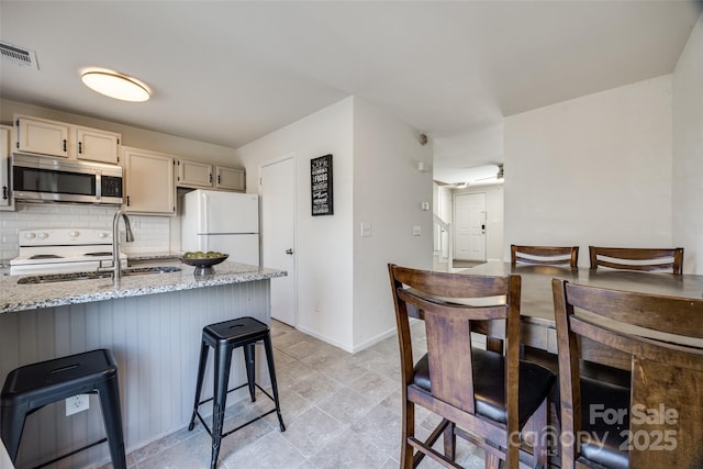 kitchen with visible vents, a sink, light stone counters, tasteful backsplash, and white appliances