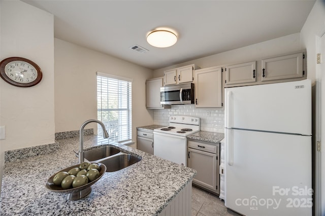 kitchen with white appliances, light stone countertops, visible vents, a sink, and tasteful backsplash