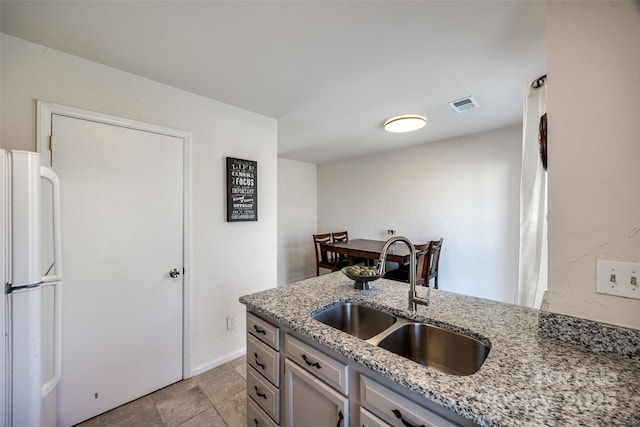 kitchen with light stone countertops, visible vents, a peninsula, freestanding refrigerator, and a sink