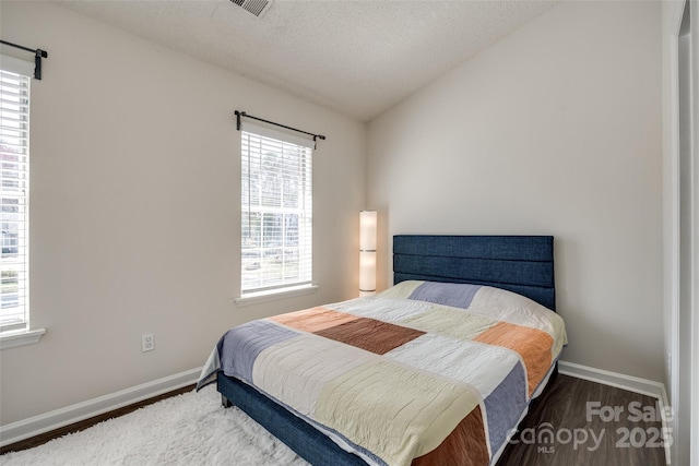 bedroom with a textured ceiling, baseboards, lofted ceiling, and wood finished floors