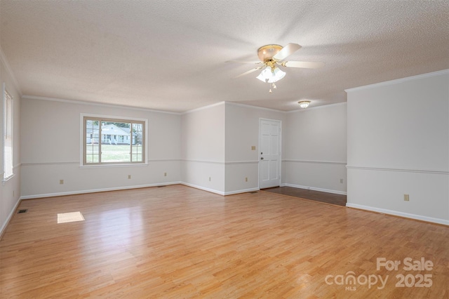 spare room featuring light wood-type flooring, ornamental molding, a ceiling fan, a textured ceiling, and baseboards