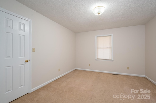 unfurnished room with visible vents, light colored carpet, a textured ceiling, and baseboards