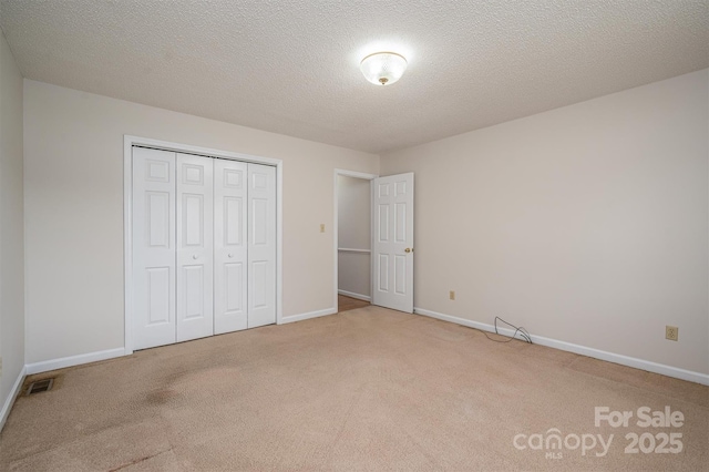 unfurnished bedroom with a textured ceiling, carpet, a closet, and baseboards