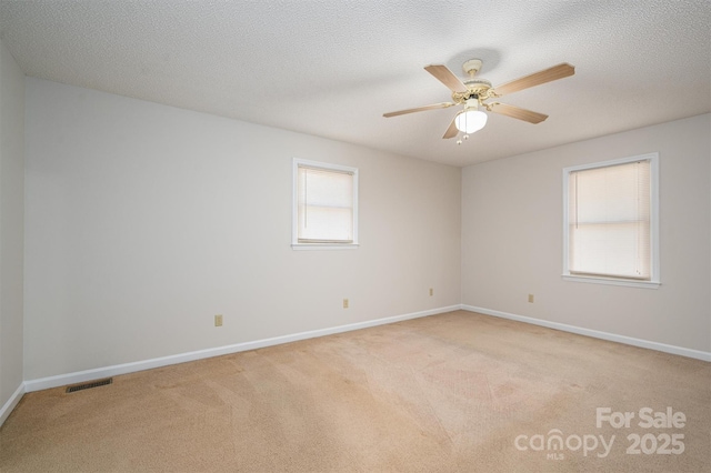 empty room with visible vents, light carpet, a textured ceiling, and baseboards