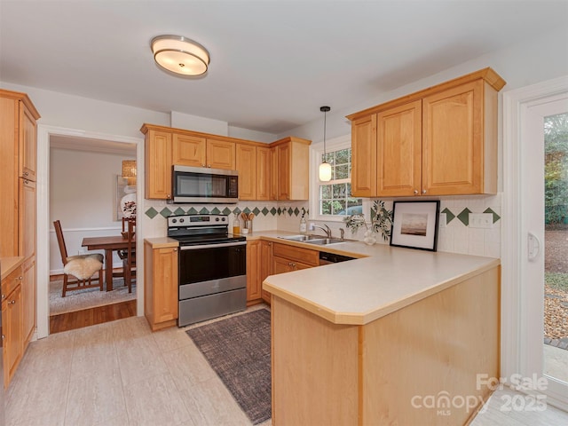 kitchen featuring a sink, appliances with stainless steel finishes, a peninsula, light countertops, and hanging light fixtures