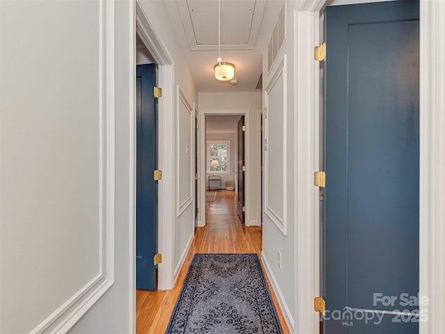 corridor featuring visible vents, attic access, light wood-type flooring, and baseboards