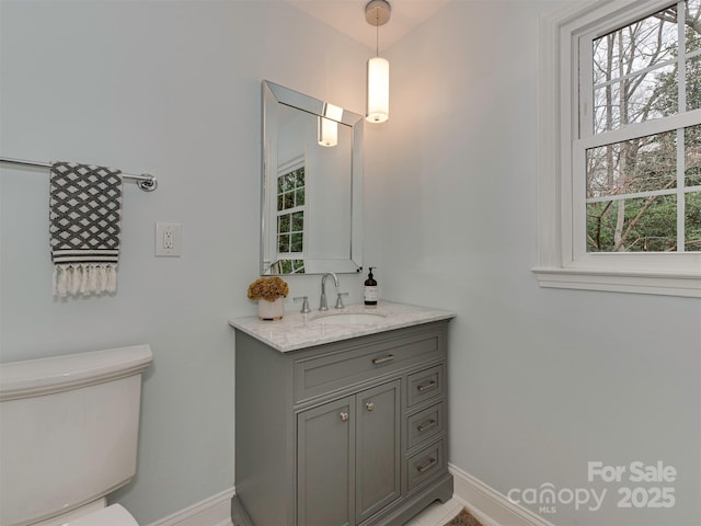 half bathroom with vanity, toilet, a healthy amount of sunlight, and baseboards