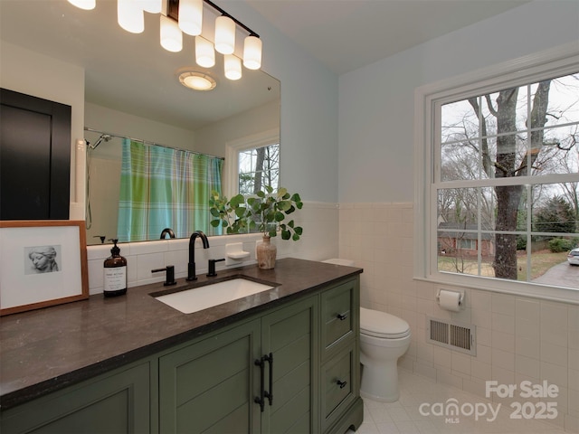 bathroom featuring visible vents, toilet, vanity, wainscoting, and tile walls