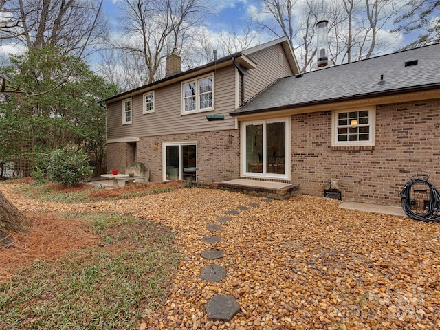 back of house featuring brick siding, a shingled roof, a chimney, and a patio area