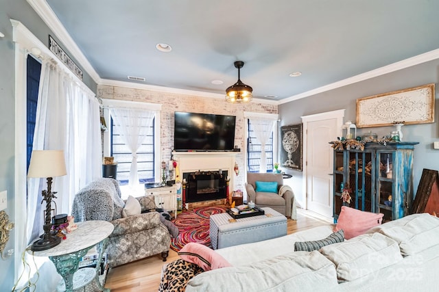 living area featuring a glass covered fireplace, crown molding, wood finished floors, and visible vents