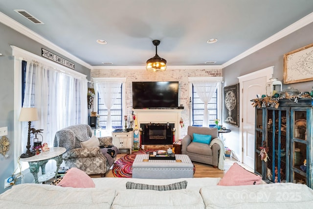 living area featuring visible vents, wood finished floors, crown molding, and a glass covered fireplace