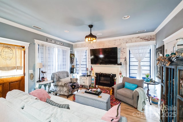 living area with visible vents, wood finished floors, ornamental molding, and a fireplace