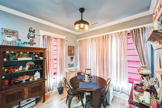 dining space with light wood-type flooring, visible vents, and ornamental molding