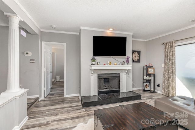 living area featuring a tiled fireplace, ornamental molding, wood finished floors, and decorative columns