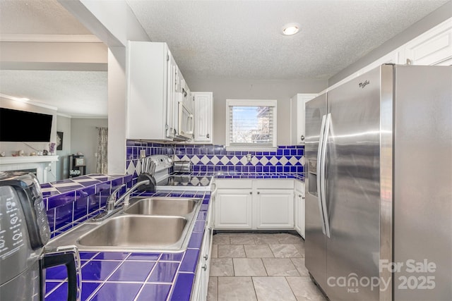 kitchen featuring a textured ceiling, tasteful backsplash, white cabinetry, stainless steel fridge, and tile counters