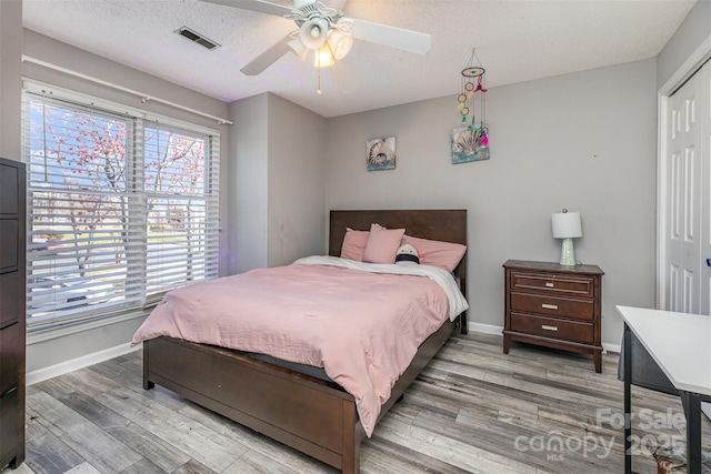 bedroom with visible vents, baseboards, a textured ceiling, and wood finished floors