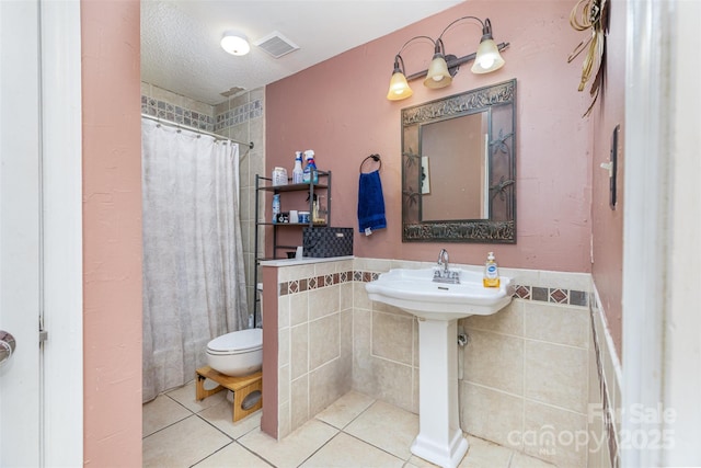 full bathroom with tile patterned floors, visible vents, curtained shower, a textured ceiling, and tile walls