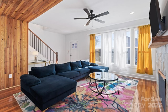 living area with wooden walls, baseboards, ceiling fan, stairs, and wood finished floors