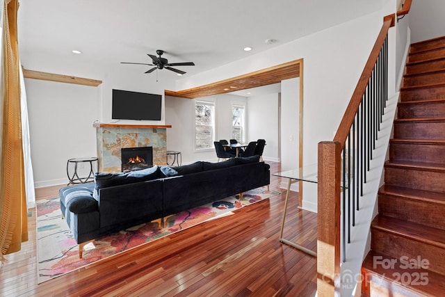 living area featuring a ceiling fan, a warm lit fireplace, hardwood / wood-style floors, recessed lighting, and stairway