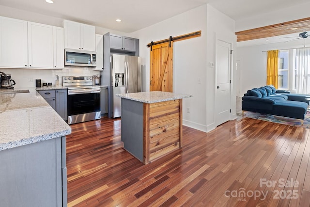 kitchen with a barn door, appliances with stainless steel finishes, open floor plan, and dark wood finished floors