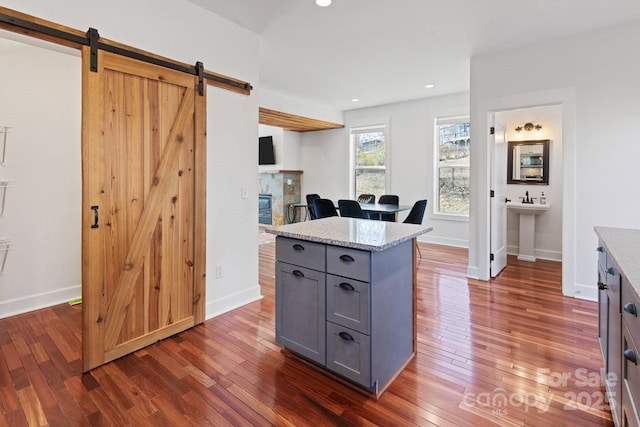 kitchen with gray cabinetry, dark wood-type flooring, a barn door, and light stone countertops