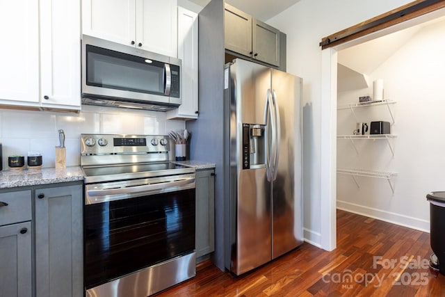 kitchen featuring light stone countertops, stainless steel appliances, dark wood-type flooring, a barn door, and tasteful backsplash