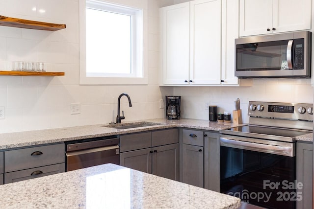 kitchen with gray cabinetry, light stone countertops, decorative backsplash, appliances with stainless steel finishes, and a sink