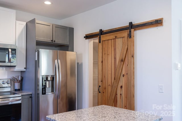 kitchen featuring a barn door, light stone counters, recessed lighting, and stainless steel appliances