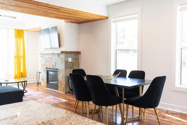 dining area featuring baseboards, a glass covered fireplace, and light wood finished floors