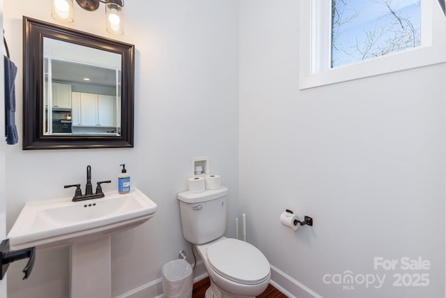 half bath with toilet, baseboards, and a sink