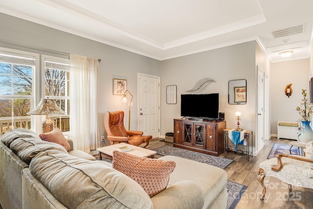 living area with visible vents, baseboards, wood finished floors, and ornamental molding