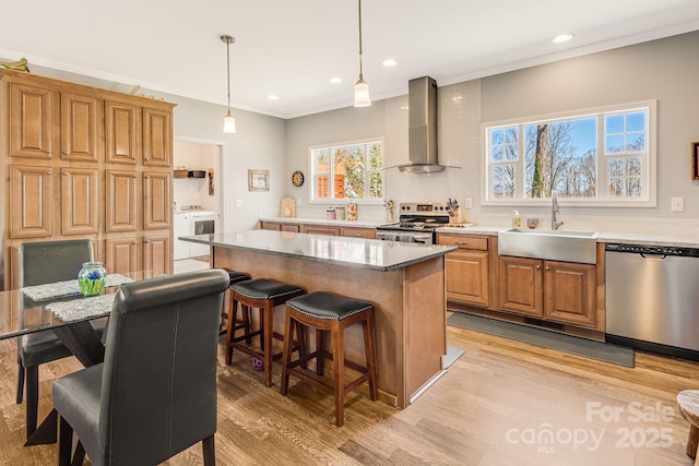 kitchen featuring a kitchen island, appliances with stainless steel finishes, washer / clothes dryer, wall chimney exhaust hood, and a sink