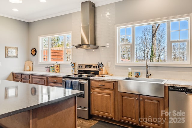 kitchen with a sink, decorative backsplash, appliances with stainless steel finishes, crown molding, and wall chimney range hood