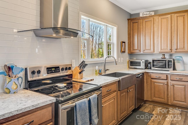 kitchen featuring ornamental molding, a sink, light countertops, appliances with stainless steel finishes, and wall chimney exhaust hood