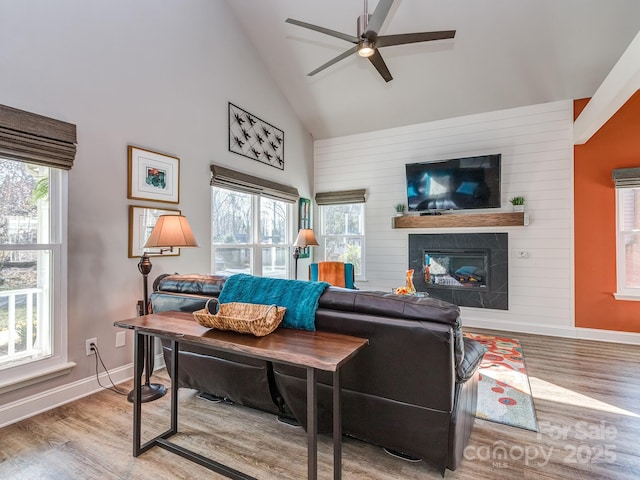 living room with high vaulted ceiling, wood finished floors, a large fireplace, baseboards, and ceiling fan